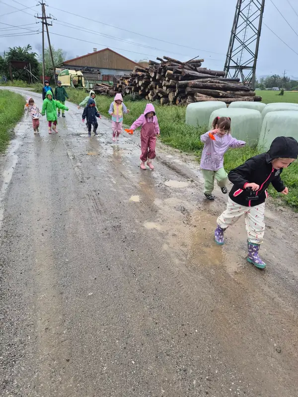 Otroci v dežnih oblačilih tečejo po mokri poti